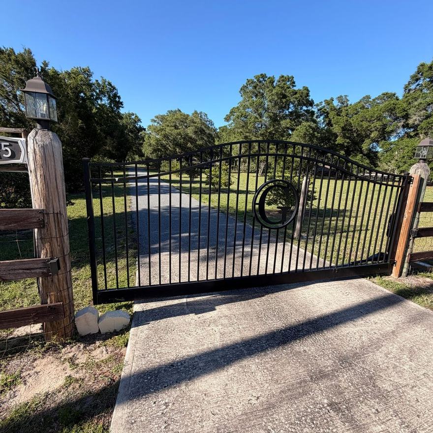 Automated ornamental iron driveway gate at the end of a residential drive