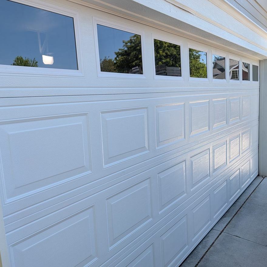 New white raised-panel garage door with window inserts installed on a home